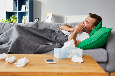 sick man blowing nose with tissues while lying on couch