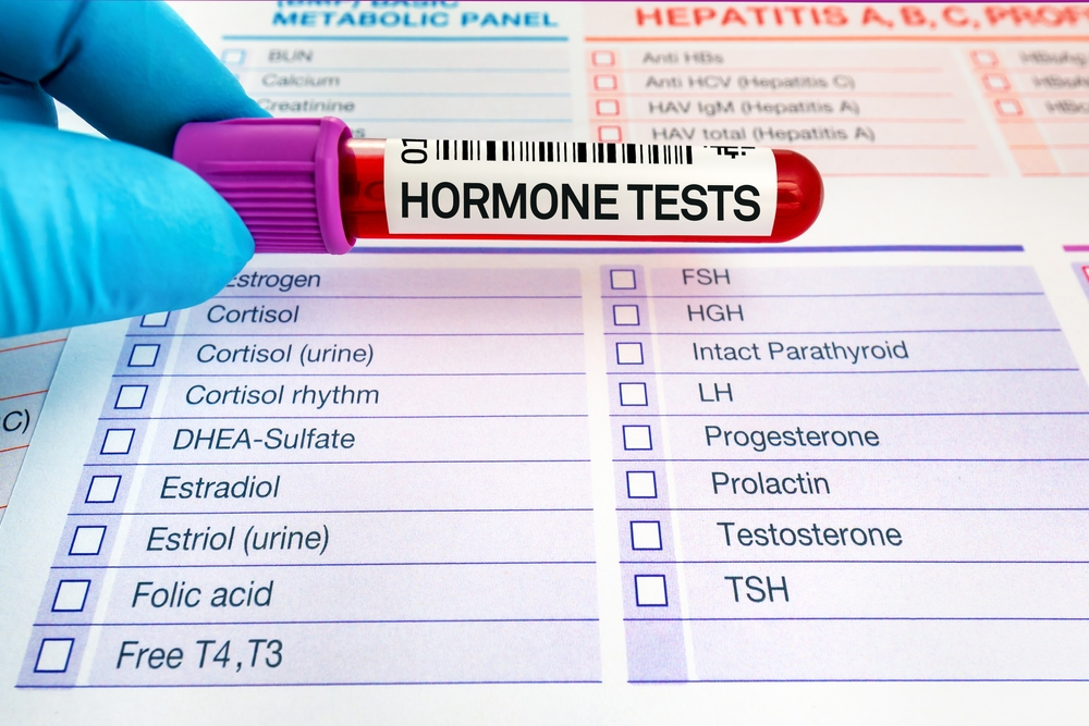 gloved hand holding blood test tube labeled Hormone Tests over list of hormones being tested